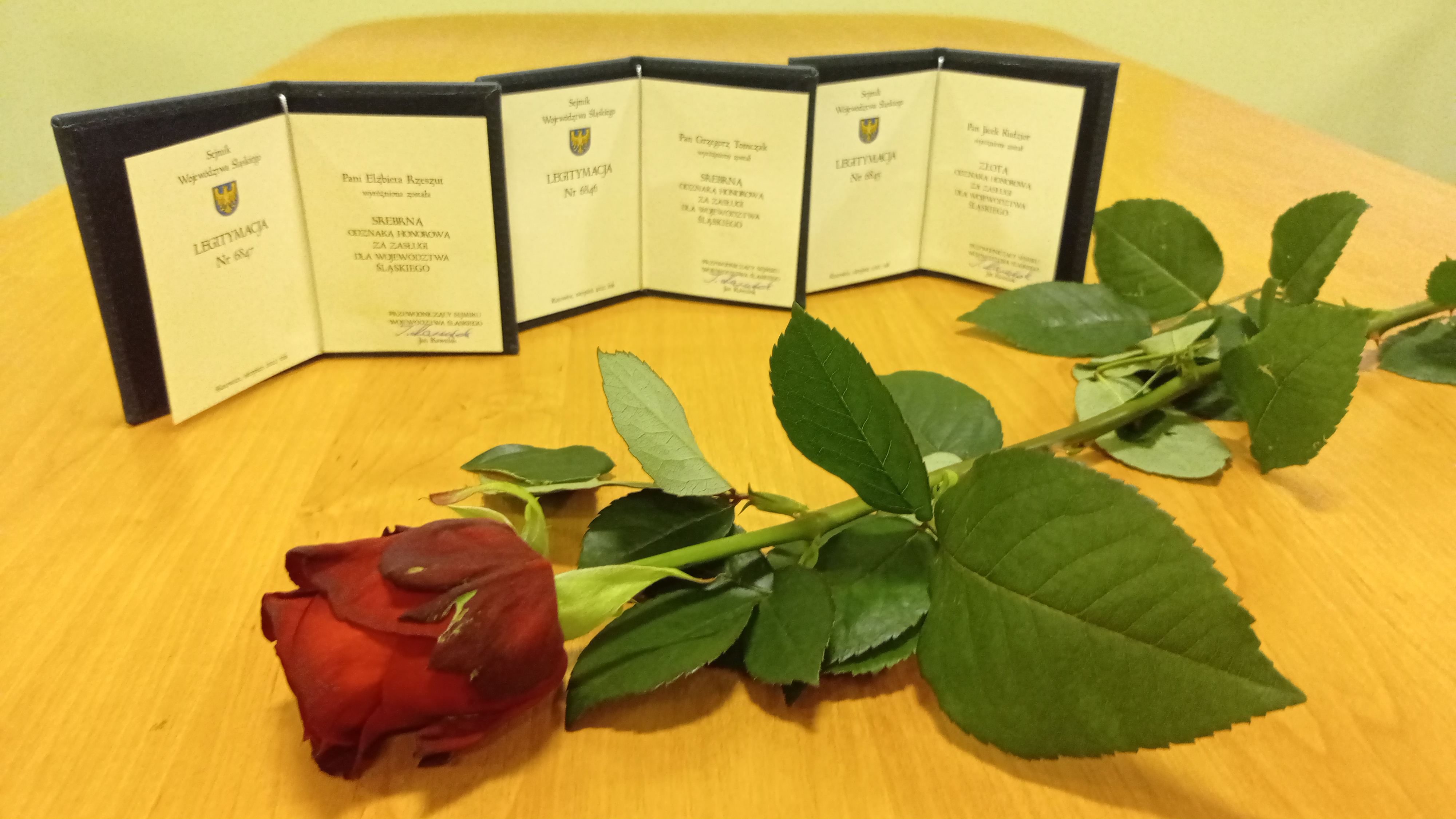Zdjęcie przedstawiające czerwoną różę oraz trzy poświadczenia otrzymania odznak.